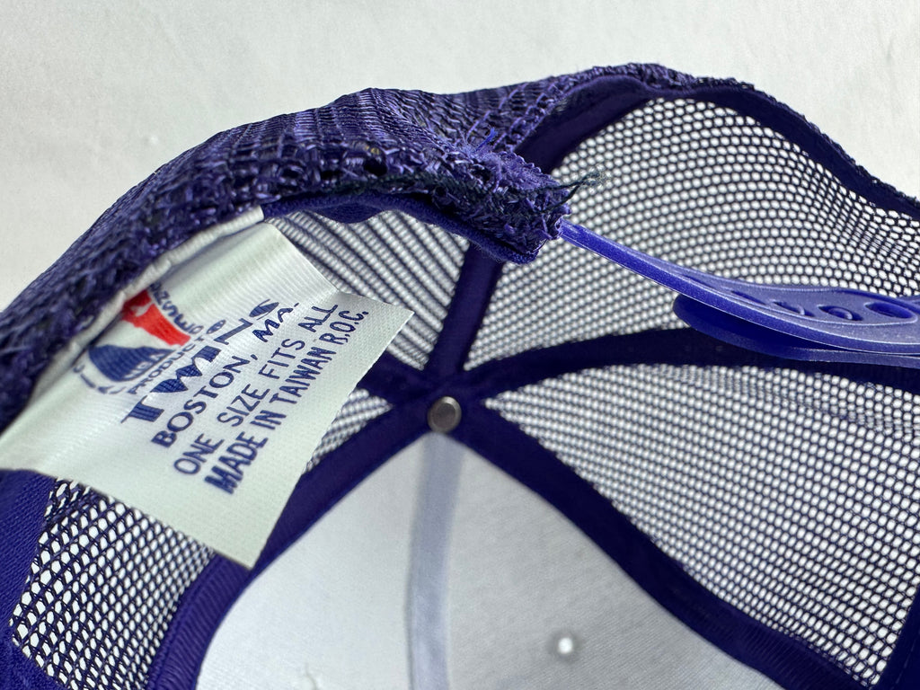 Close-up of the inside crown of a Twins, Boston, MA brand trucker hat, showing the purple mesh back, embroidered logo patch, and white size tag.
