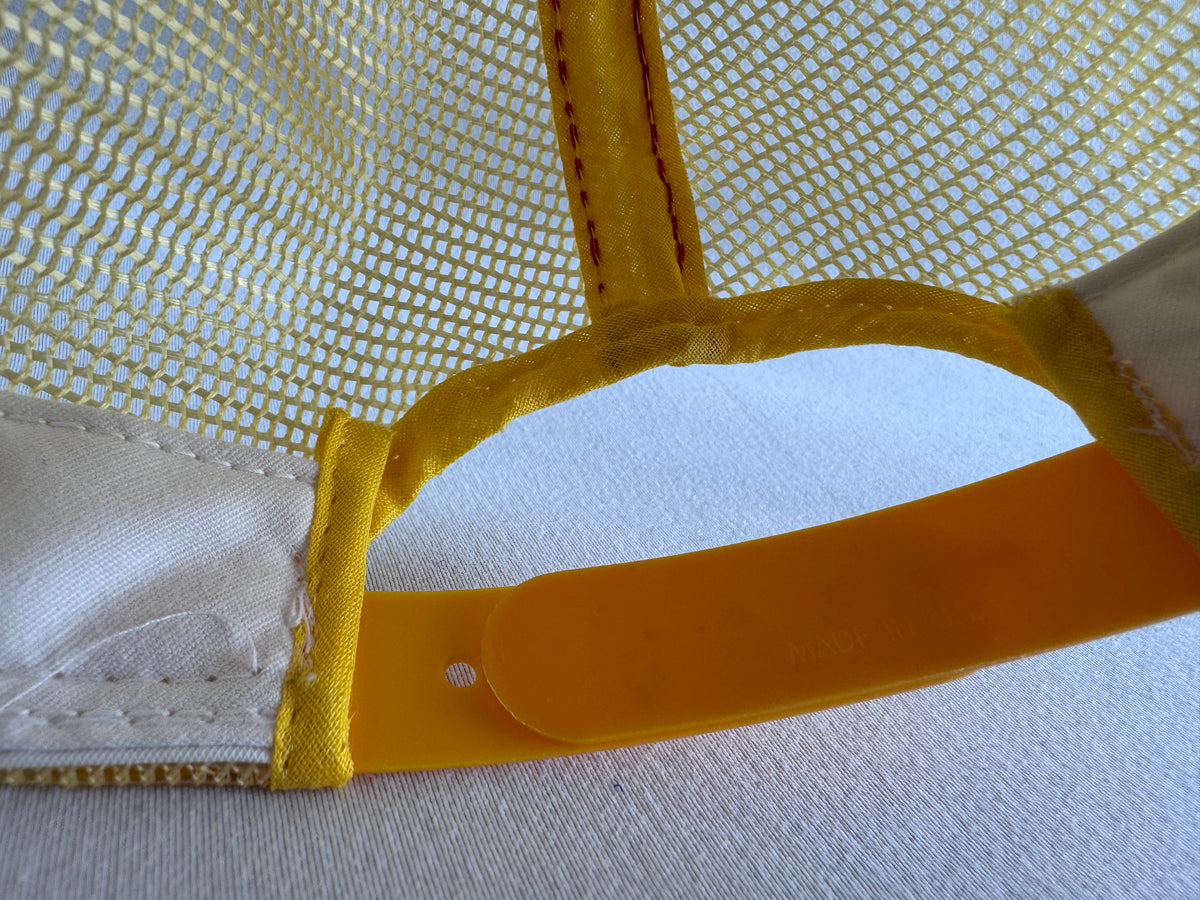 Close-up detail of a yellow and white mesh cap showing the back strap attachment and yellow fabric trim.