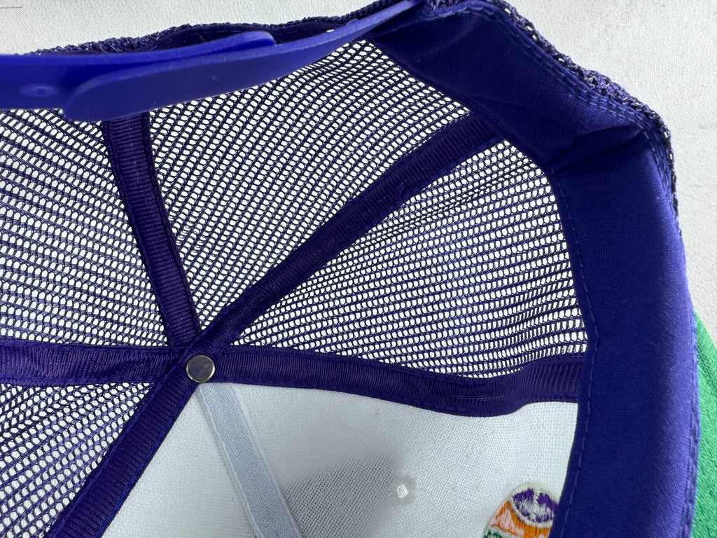 Close-up of the inside crown of a trucker-style cap, showing a purple mesh back, purple fabric brim, and a small multicolor embroidered patch near the lower right edge.