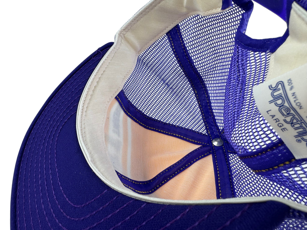 Close-up of the back of a purple mesh trucker cap with a white interior lining and a visible AJD Superstripe tag.