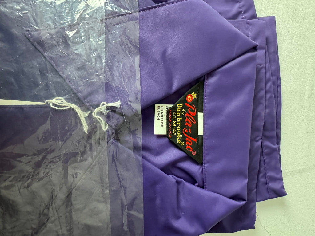 A folded purple nylon jacket shown with its clear plastic garment bag on the left and a black interior label reading 'Pla-Jac by Dunbrooke'  on the right.