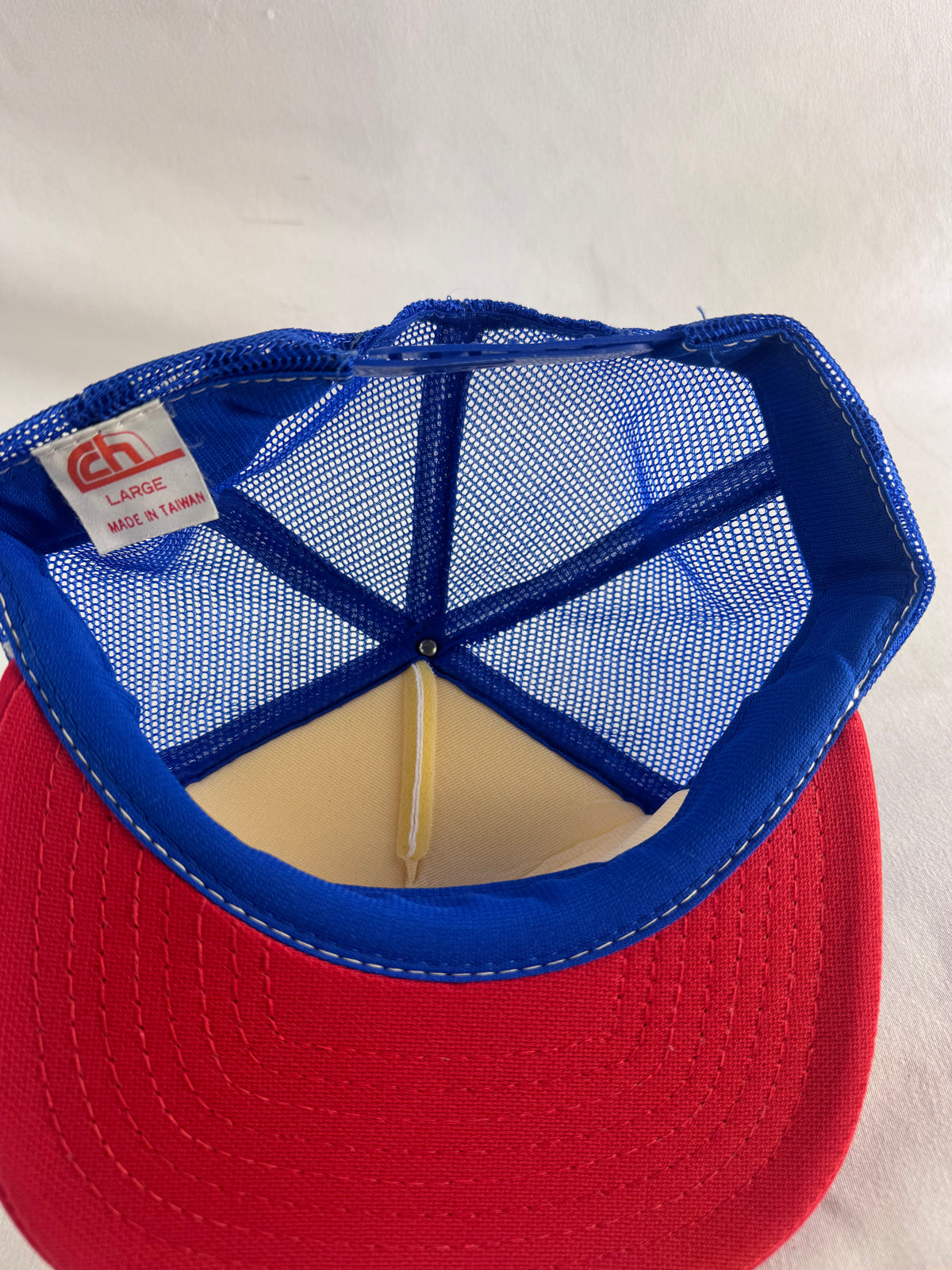 A red and blue trucker-style cap viewed from the back, showing a blue mesh back, blue fabric trim, and a red brim with white stitching.