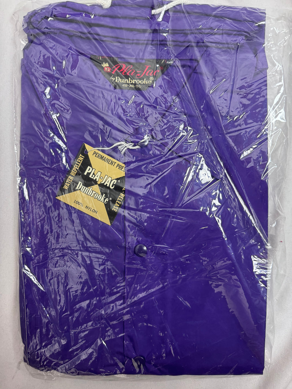 A purple Pla-Jac Dunbrooke nylon jacket packaged in clear plastic, featuring a black and red brand label and a black and gold hangtag.