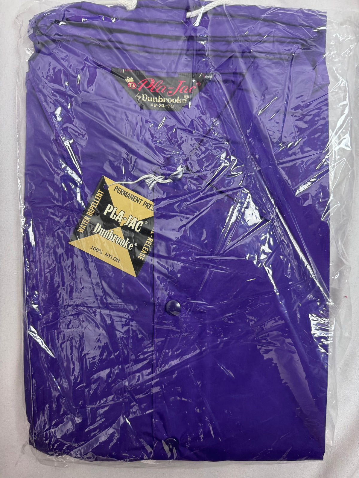 A purple Pla-Jac Dunbrooke nylon jacket packaged in clear plastic, featuring a black and red brand label and a black and gold hangtag.
