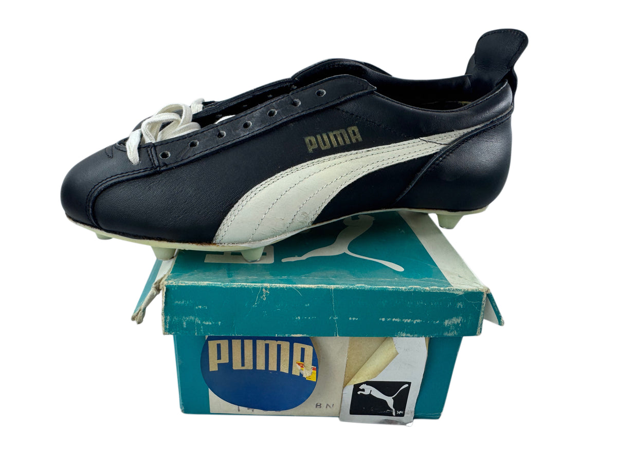 A vintage Puma leather soccer cleat in black and off-white, displayed on top of its teal and white Puma shoebox against a white background.