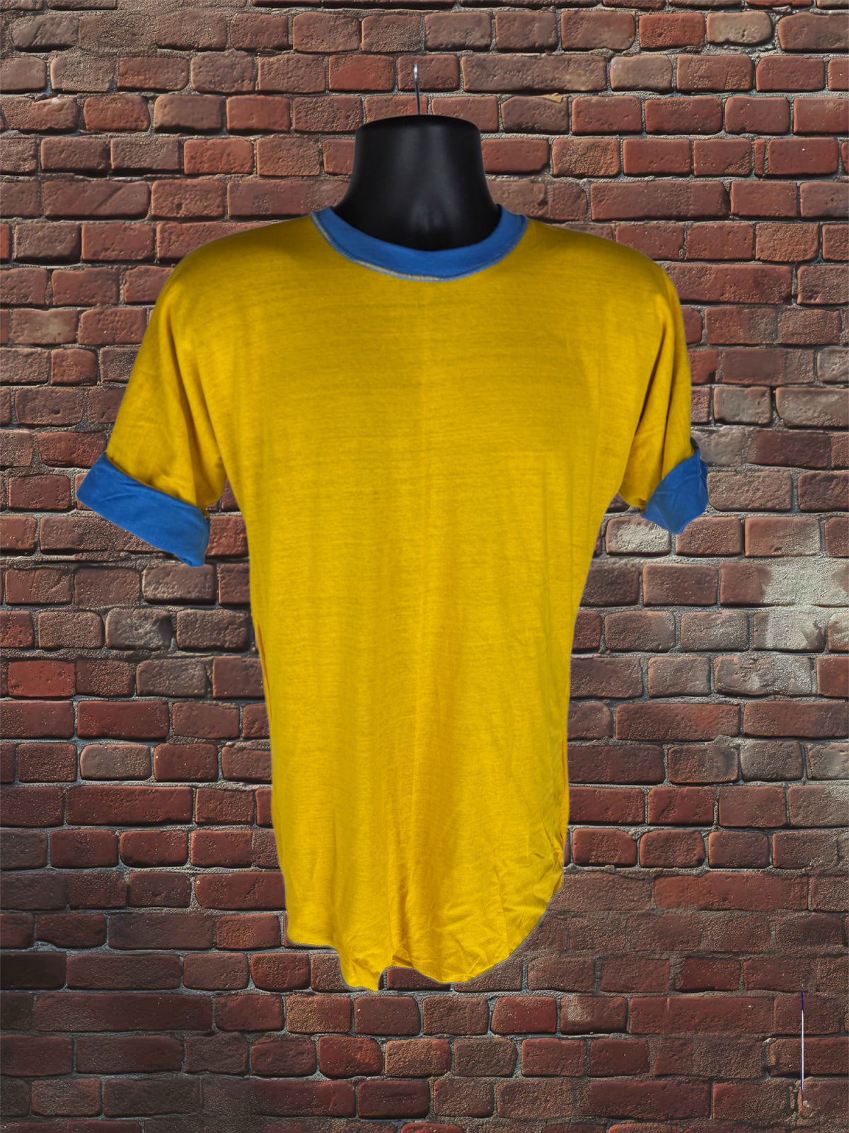 A yellow short-sleeve t-shirt with blue trim on the collar and cuffs, displayed on a black mannequin torso against a red brick wall background.