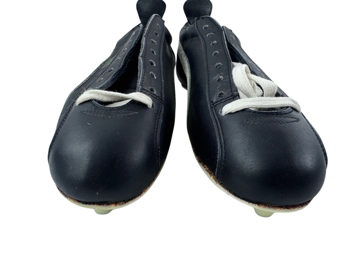 A pair of vintage black leather soccer/football shoes with white laces and white rubber tips, shown against a plain white background.