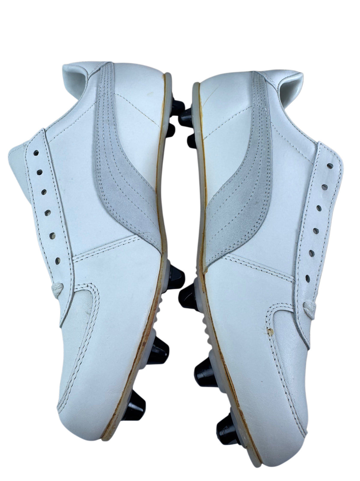 A pair of white leather athletic cleats shown from the side, featuring black rubber studs on the soles and light tan outsoles, set against a plain white background.